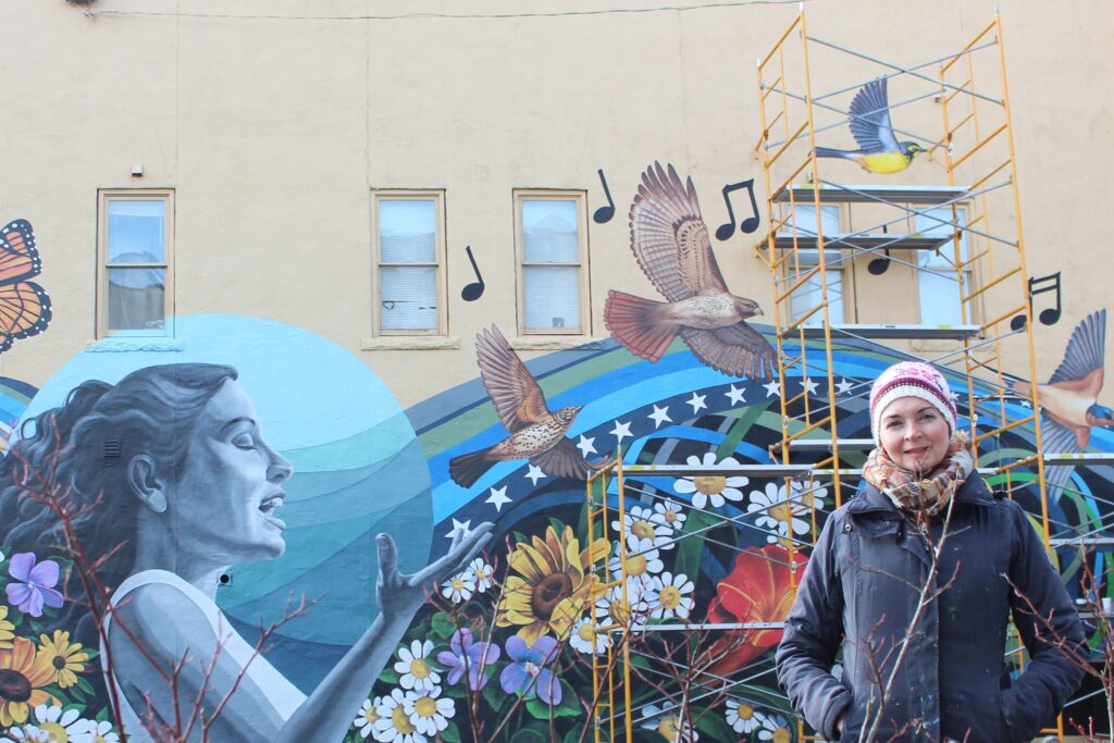 Local artist Jamie Corum stands in front of the mural she painted at the site of the Levitt AMP Middlesboro Music Series. 